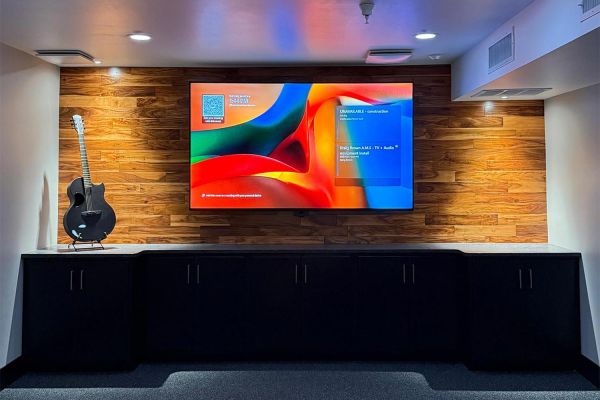 Large screen mounted on a wood accent wall above dark cabinets with a guitar